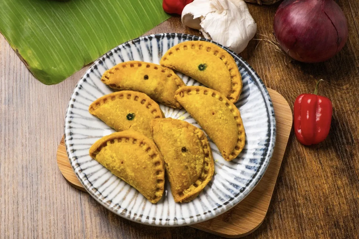 Plate of golden hand-crimped vegan patties with scotch bonnet peppers, garlic and red onion